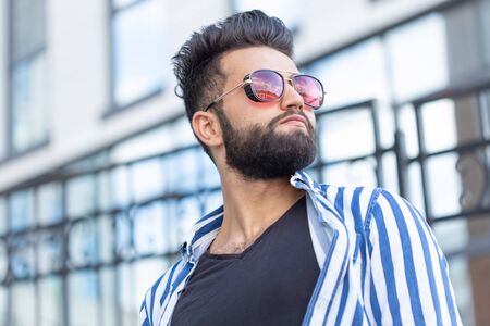 Portrait of cheerful positive stylish student guy in glasses with a mustache and beard outdoors. The...