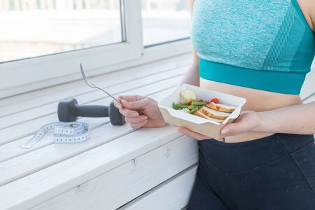 sport, healthy, people concept - Close-up of girl holding salad and dumbbell after fitness trainingの写真素材