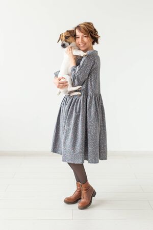 Charming smiling young woman in a stylish gray dress holding her favorite dog Jack Russell Terrier. Concept favorite dogs.の写真素材