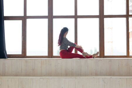 Daydreaming, thoughtfulness and loneliness concept - Young caucasian woman sitting in her living room and looking out through big windowの写真素材