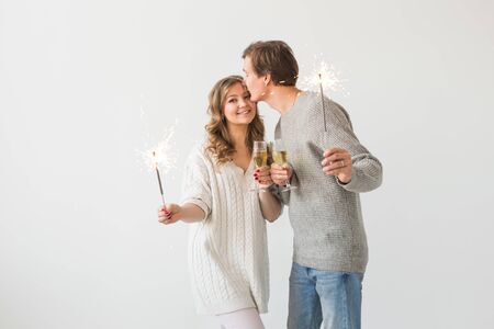 New year, holidays, date and valentines day concept - Loving couple holding sparklers light and glasses of champagne over white backgroundの写真素材