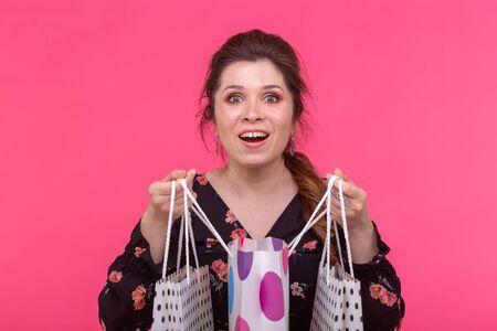 Positive young stylish woman holding bags posing on a pink background. Shopping concept in a mall.
