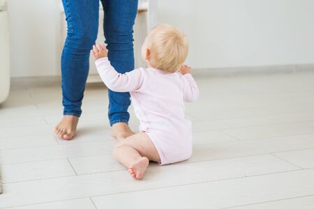 Little crawling baby girl one year old sitting on floor in bright light living room smiling and...