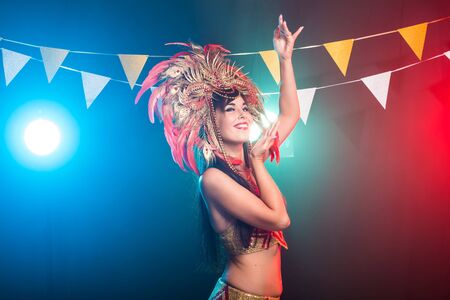Cabaret, dancer and holidays concept - Cute young girl in bright colorful carnival costume on dark...