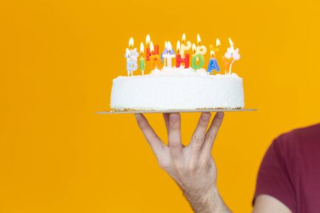 Hands holding a birthday cake with candles and the inscription birthday on a yellow background. Congratulations on the anniversary and birthday. Copyspace.の写真素材