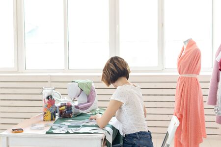 Positive young pretty girl seamstress designer working on a new project while sitting at her desk with a sewing machine in her workshop. Creative business concept.の写真素材