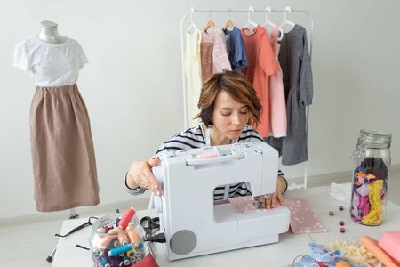 Young talented woman designer clothes sews her new product sitting at her desk with sewing machine...