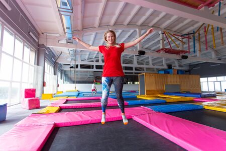Fitness, fun, leisure and sport activity concept - Young happy woman jumping on a trampoline indoorsの写真素材