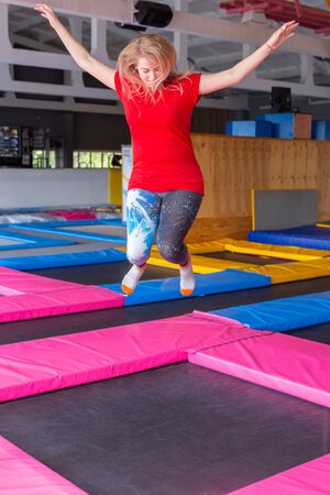 Fitness, fun, leisure and sport activity concept - Young happy woman jumping on a trampoline indoorsの写真素材