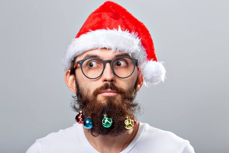 Christmas, holidays, barbershop and style concept - young handsome bearded santa claus man with many small christmas baubles in long beardの写真素材
