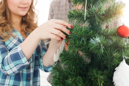 family, x-mas, winter holidays and people concept - close-up of happy young couple decorating christmas tree at homeの写真素材