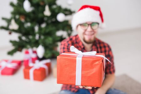 Christmas and holidays concept - Funny man in santa hat holding a gift at home in the living roomの写真素材