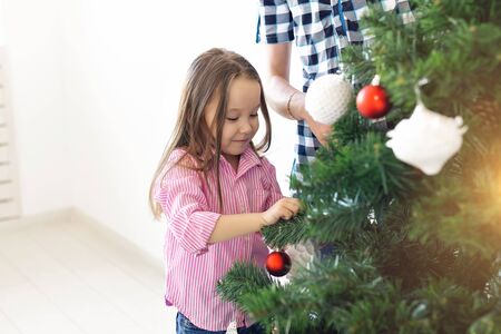 Holidays, parents and celebrating concept - Happy family decorating a Christmas tree with baubles in the living-room on white backgroundの写真素材