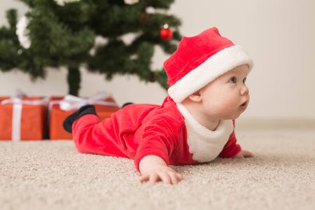 Cute baby girl wearing santa claus suit crawling on floor over Christmas tree. Holiday season.の写真素材