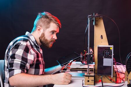 Young male designer engineer using a 3D printer in the laboratory and studying a product prototype,...