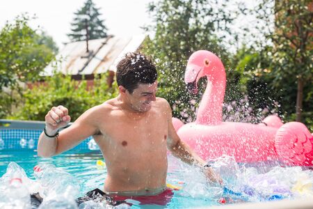 Ecology, plastic trash, environmental emergency and water pollution - shocked man standing in a dirty swimming pool.の写真素材