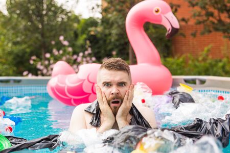 Ecology, plastic trash, environmental emergency and water pollution - shocked man swim in a dirty swimming poolの写真素材