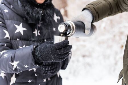 Bottle and cold season concept - Close-up of man pours a hot drink. Couple on a winter holidayの写真素材