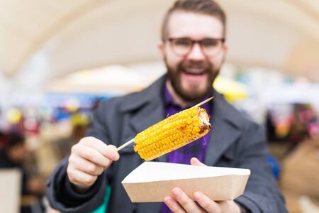 Street food and cuisine concept - Man eating grilled corn. Vegetarian food. Healthy and tasty...