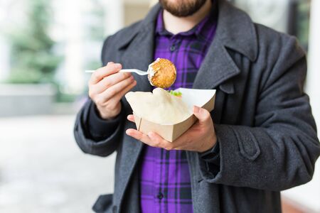 Junk food, eating and lifestyle concept - close up of young man with meal eats on city streetの写真素材