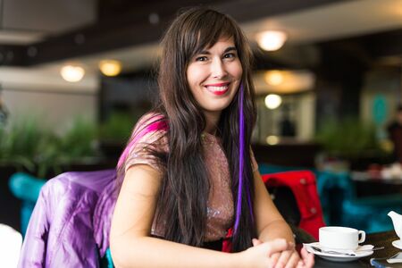 Young stylish trendy woman with multi-coloured strand in hair sits in cafeの写真素材