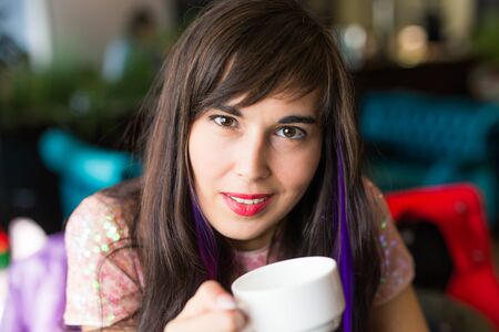 Portrait of young stylish trendy woman with multi-coloured strand in hair sits in cafe