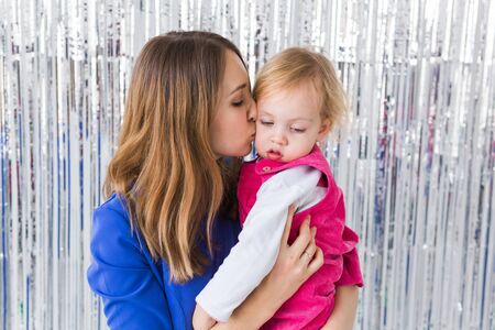 Childhood, holidays and family concept - Mother kissing baby daughter on shiny background. Close-upの写真素材