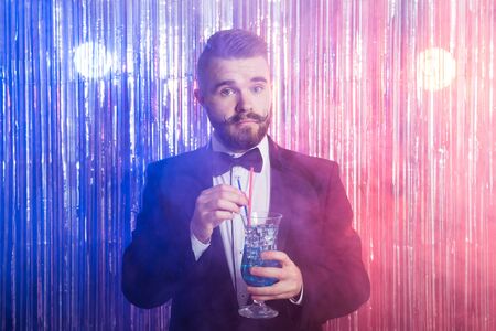 Club party and holidays concept - Portrait of elegant handsome man in a expensive suit holds blue cocktail on shiny background.の写真素材