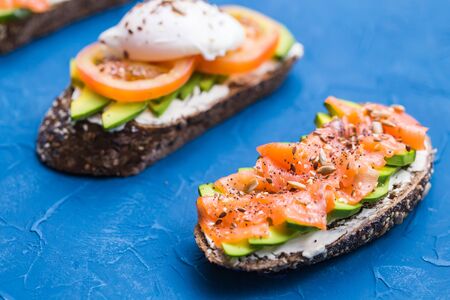 Sandwiches with smoked salmon, eggs, sauce and avocado on blue background. Concept of breakfast and healthy nutritionの写真素材