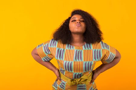 Young beautiful african american girl with an afro hairstyle. Portrait on yellow background. Girl looking at camera.の写真素材