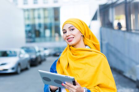 Arab woman student. Beautiful muslim female student wearing bright yellow hijab holding tablet.の写真素材