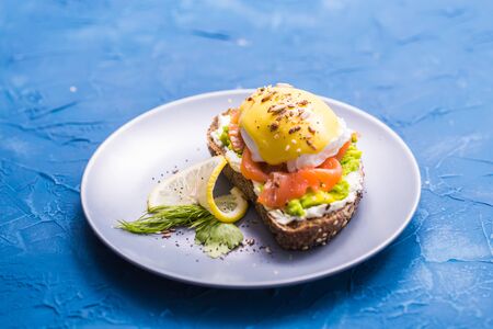 Sandwich with smoked salmon, egg and avocado on blue background, close-up. Concept for healthy...