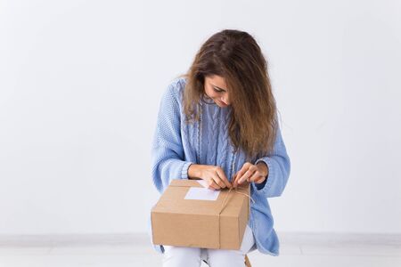 Delivery and fashion concept - Woman sitting on sofa at home opening online clothing purchaseの写真素材