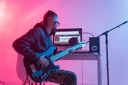 Create music and a recording studio concept - Bearded man guitarist recording electric bass guitar track in home studioの写真素材