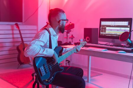 Create music and a recording studio concept - Bearded funny man guitarist recording electric bass guitar track in home studioの写真素材