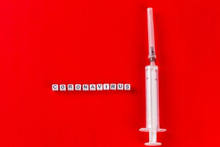 Pandemic and virus concept - Coronavirus text with syringe on red background. Novel coronavirus...