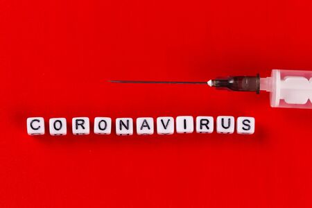 Pandemic and virus concept - Coronavirus text with syringe on red background. Novel coronavirus Covid-19.の写真素材