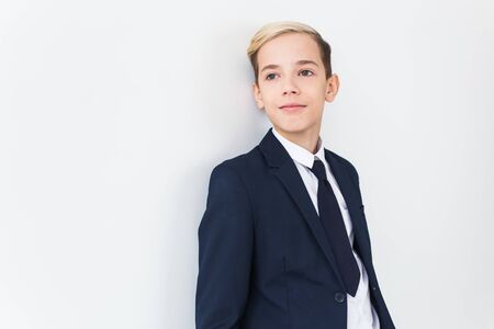 Portrait of stylish school boy teenager in white shirt and jacket against white background with copy space.の写真素材