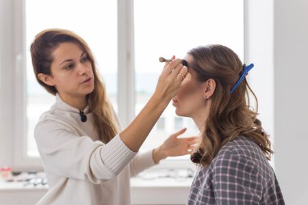 Beauty and cosmetics concept - Make-up artist doing professional make up of young woman
