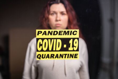 Coronavirus, quarantine, covid-19 and pandemic concept. Sad and sick woman of corona virus looking through the window. Stay at home.の写真素材