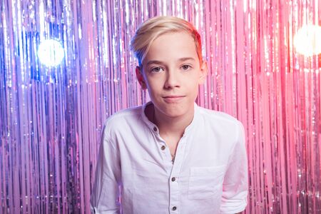 Awkward age and teenage concept - Portrait of teen boy at a party. Shiny background.の写真素材