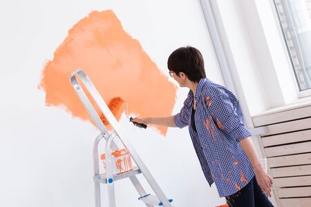Renovation, redecoration and repair concept - middle-aged woman painting wall in new apartment.の写真素材