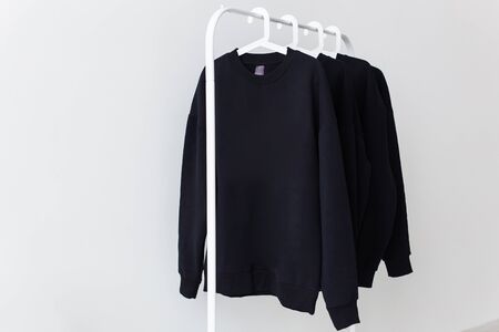 Sweatshirts and hoodies hanging on hangers in the store. Street fashion, unisex and youth wearsの写真素材