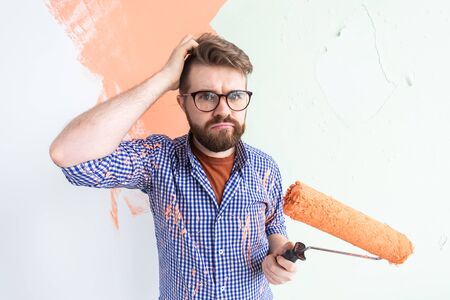 Funny confused man painting interior wall of home. Renovation, repair and redecoration concept.の写真素材