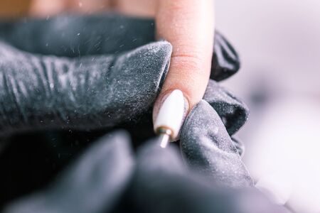 Close-up of hardware milling cutter for removing gel polish. Apparatus manicure in beauty salon. Manicurist with electric nail drill remove old gel from client nails. Process of replacing shellac.の写真素材