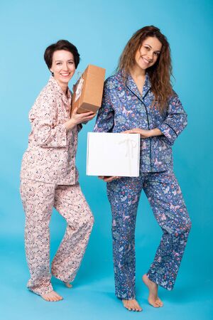 Portrait of three beautiful young girls wearing colorful pyjamas having fun during sleepover isolated over blue background. Pajama party and hen-party conceptの写真素材