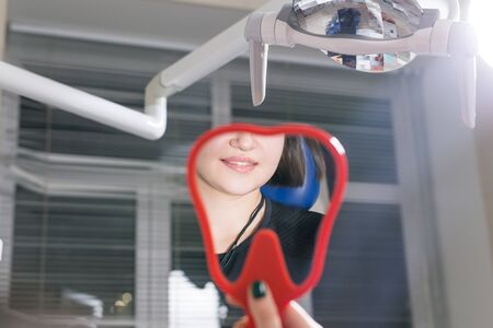 Female checking teeth in mirror. Smiling woman at dentist office. Smile wider and be beautiful.