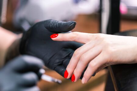 CloseUp shot of master in rubber gloves covering red nails with top coat in the beauty salon. Perfect nails manicure process.の写真素材