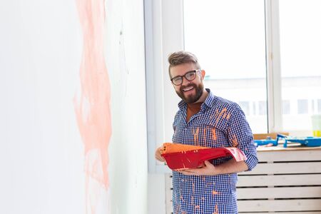 Happy man painting interior wall with paint roller in new house. Guy with roller applying paint on a wall.の写真素材