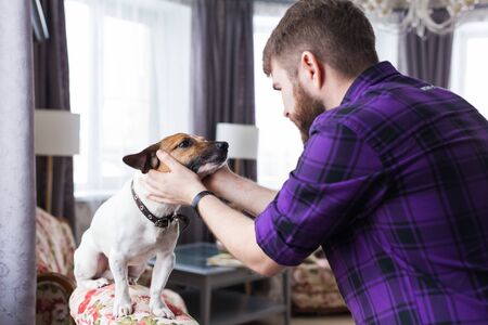 Happy young man sitting with his dog at home. Pet owner, animals and friendship concept.